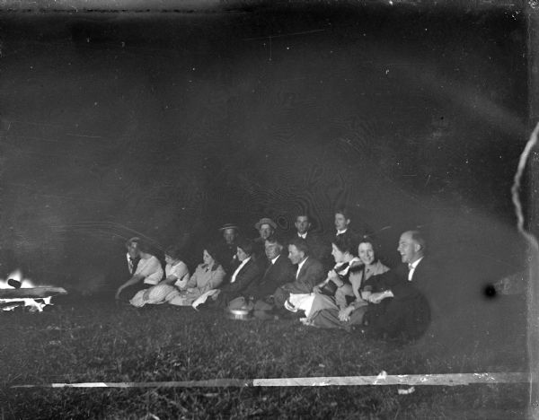Outdoor group portrait of young men and women sitting near a campfire.