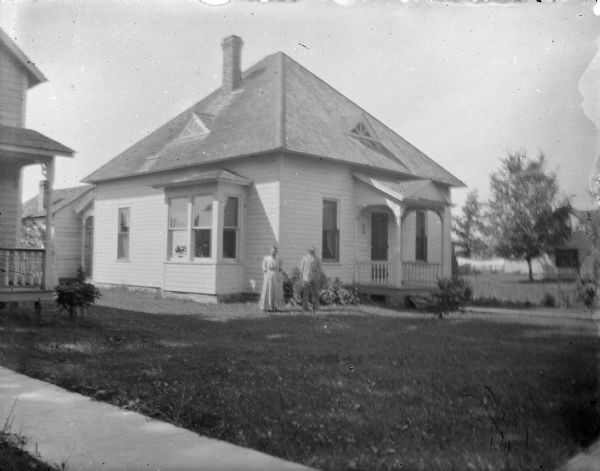 Outdoor portrait of a man and woman posing standing in the yard in front of a wooden house.