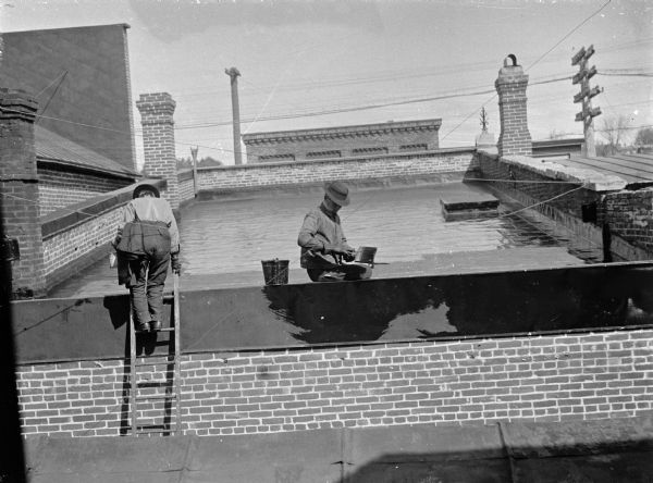 View from roof towards two men working on the roof of another building.