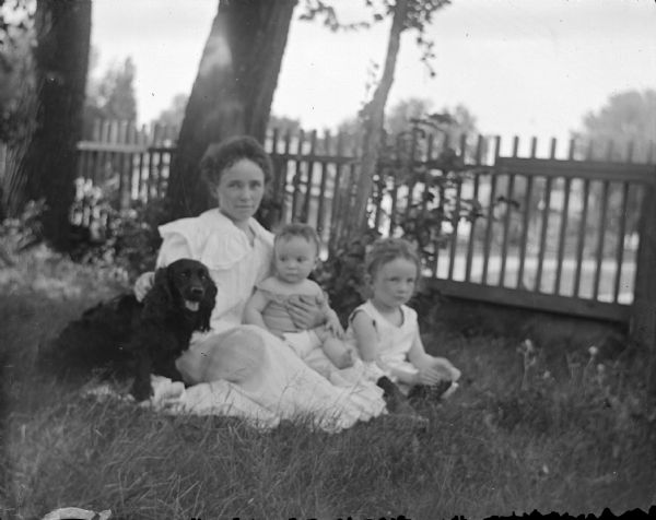 Outdoor group portrait of a woman, two children, and a dog posing sitting on the grass in a yard.
