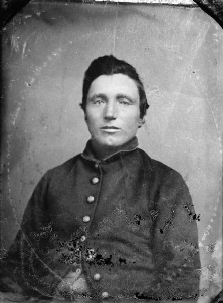 Copy photograph of a waist-up studio portrait of a man posing sitting and wearing a dark-colored coat. Original photograph has oval marks around the man.
