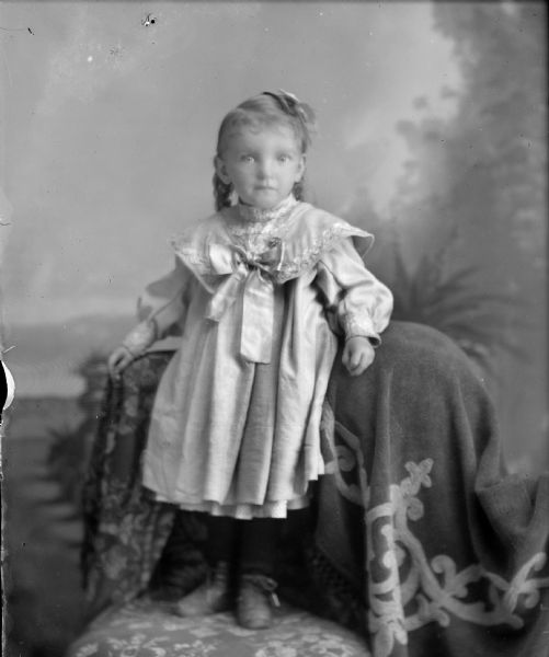 Studio portrait of girl posing standing on a chair wearing a light-colored dress.