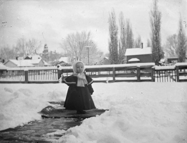 Outdoor view of a girl posing standing on a walkway in a snow-covered yard.