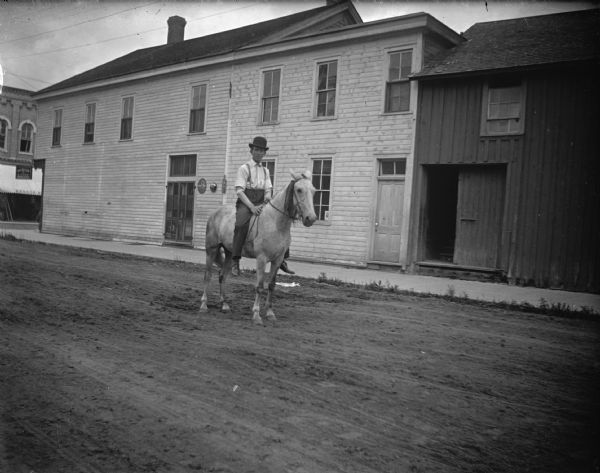 Outdoor view of a man posing sitting on a horse on a town street. Location identified as South First Street in Black River Falls.
