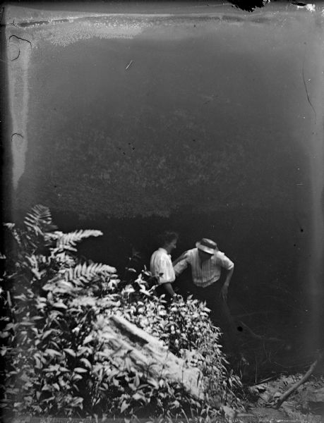 Outdoor view of a man and woman standing by wild vegetation. Possibly at a riverside.