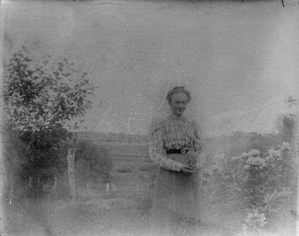 Outdoor view of a woman posing standing by a flowering bush.