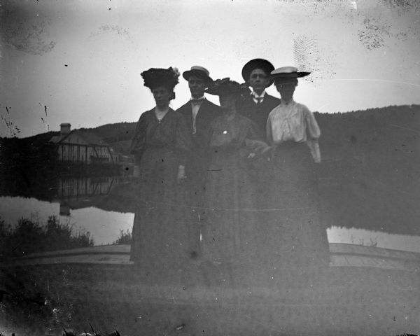 Outdoor view of a three women and two men posing standing on bluffs over a river, and buildings.