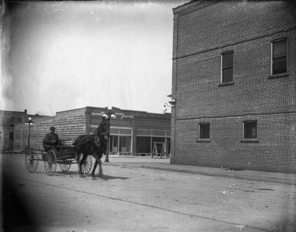 View across street towards a man driving a wagon pulled by a horse on First Street after the flood.
