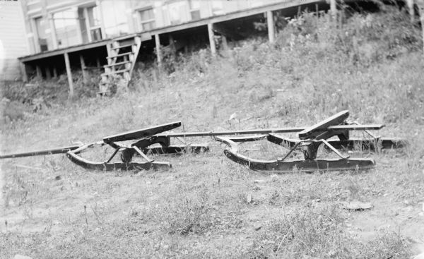 Sled runners on the grass. Location identified as the Spaulding Manufacturing yard. Part of a building and what may be a loading dock is in the background.
