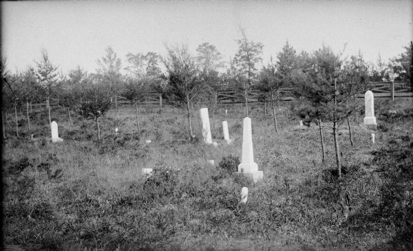 View of a small cemetery with marble markers. A large fence is in the background.