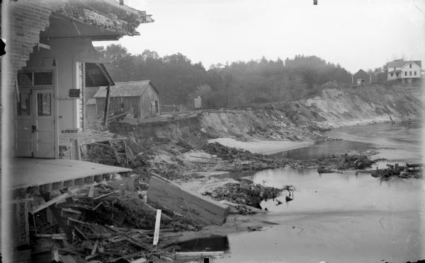 View along shoreline of damage from the 1911 flood of the Black River. An entire wall of a building is gone, and debris is along the river banks.