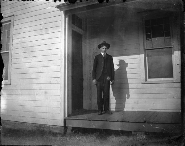 Outdoor portrait of a European American man posing standing on the porch of a wooden house.