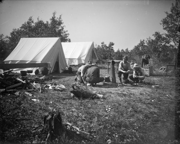 Outdoor view towards five men posing kneeling in front of two tents.
