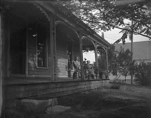 Outdoor view of two women sitting on the porch of a wooden house. The woman sitting on the left is identified as Ida Beatty Van Schaick, the wife of Charles J. Van Schaick.