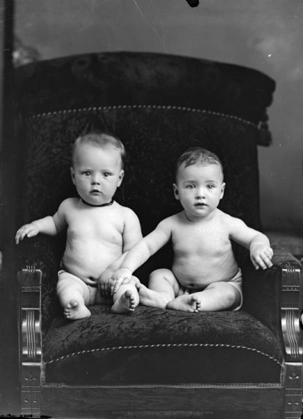 Studio portrait of two infants posing sitting on a chair.