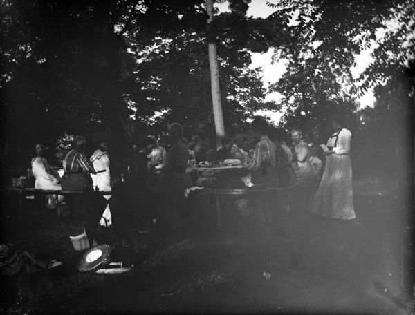 Outdoor view of a large group of women sitting around a table under the shade of trees.
