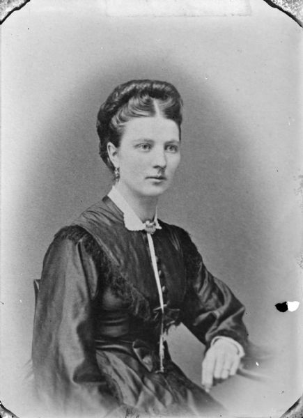 Copy photograph of a waist-up studio portrait of a woman posing sitting. She is wearing a dark-colored dress.