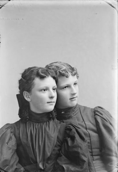 Waist-up studio portrait of two young women wearing dark-colored blouses.