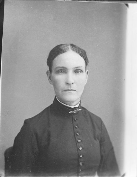 Copy photograph of a studio portrait of a European American woman posing sitting. She is wearing a dark-colored button-down jacket, collar pin, and light-colored shirtwaist.