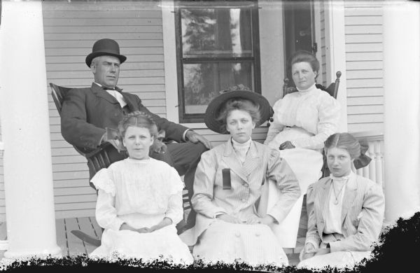 Outdoor group portrait of a European American family group posing on the porch of a house porch. The group includes a man and four women.