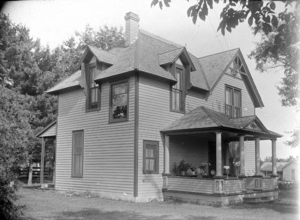 View across lawn towards the left and front sides of a two-story wood-frame house. Vases of flowers and potted plants are on the front porch. Identified as the residence of William O'Hearn, later Dr. Kalling; located at the southwest corner of North 5th Street and Monroe Street.