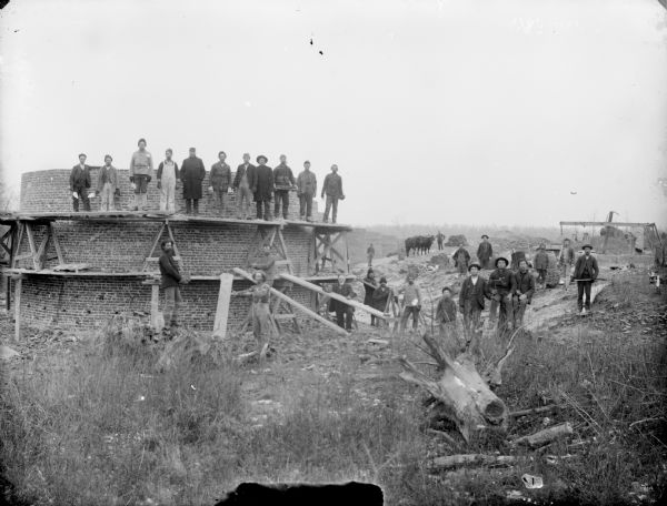 A brick structure is under construction with a large group of people posing next to it.