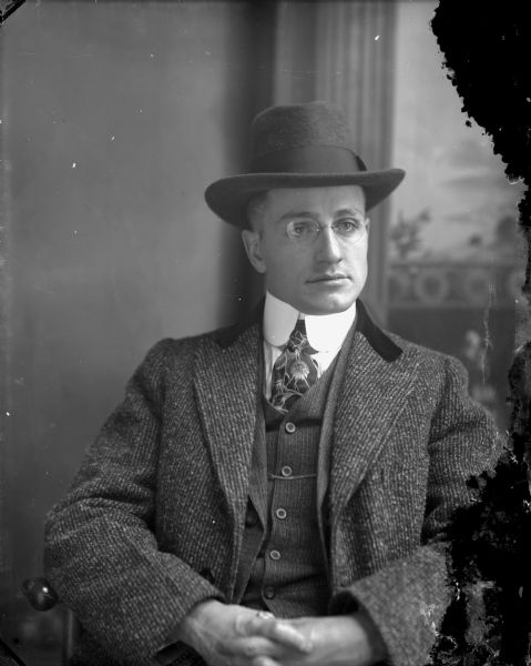 Studio portrait of a European-American man dressed in a suit and hat. He is wearing pince-nez eyeglasses. Identified as Harold Van Schaick.