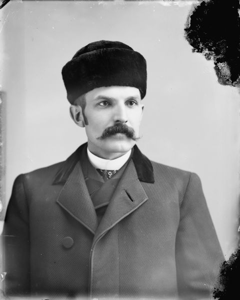 Studio portrait of a European-American man posing sitting. He is wearing a suit and a fur hat. Identified as Thomas J. Van Schaick.
