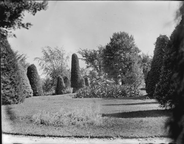 View of the lawn of the Spaulding residence with a well-manicured yard with sculpted shrubs. There is a flower bed in the center.