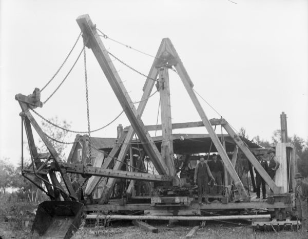 View of large machinery with four workmen standing on it. Identified as Gebhardt's Walking Cranberry Dredge.