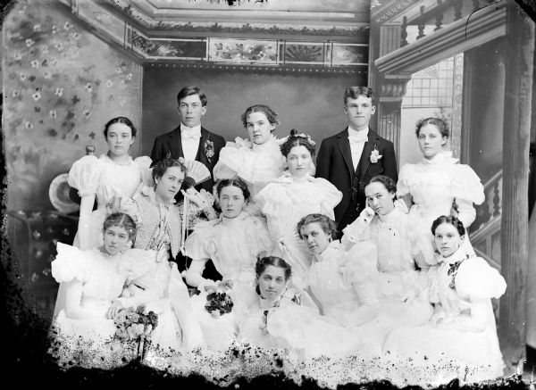 Group portrait in front of a painted backdrop of two men and ten women. Identified as a class of 1897. Back row: Ella Steihl, Carl Ogden, Myrta Crosly, Nord Sandahl, Constance Emerson. Center row: Blanche Argyle, unknown, unknown, Lulu Thompson. Front row: Grace Jones, Chloe Areston, unknown, Olava Gullard.