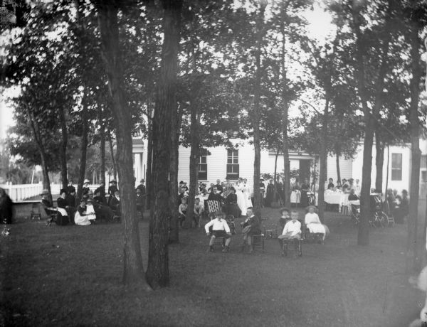 Elevated group portrait of a large gathering of people on a lawn in front of a house. Identified as a picnic at the W.T. Murray home.
