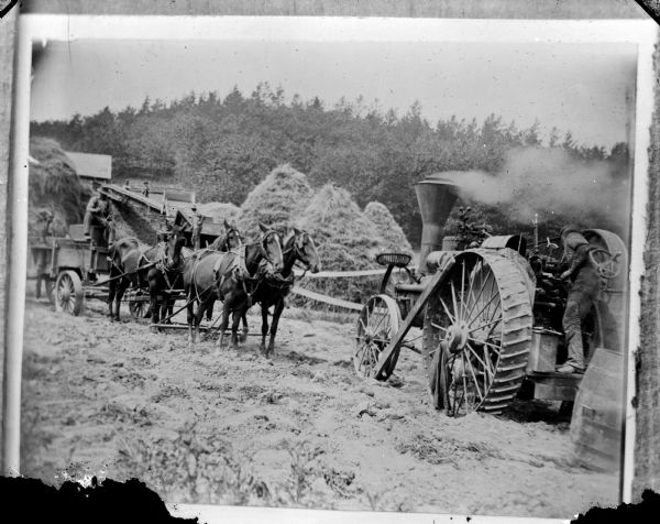 Copy photograph of a farm crew using a steam tractor and separator. Haystacks are in the background.