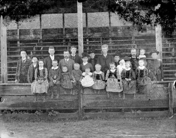 Group portrait of an extended family posing at a fence in front of grandstand benches.