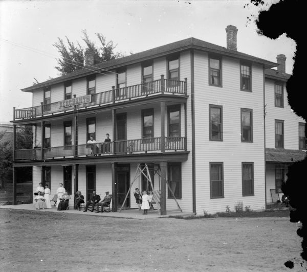 Exterior view of Merchant's Inn located at the southwest corner of S. First Street and Fillmore. Two women sitting on the second floor balcony. A group of women and men gathered near the front entrance.