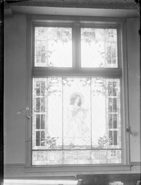 Interior view of a stained-glass window with an image of a virgin. Placed in memory of Dudley Spaulding. Identified as an east side window in the Methodist Church located at the corner of Fourth and Harrison Streets.