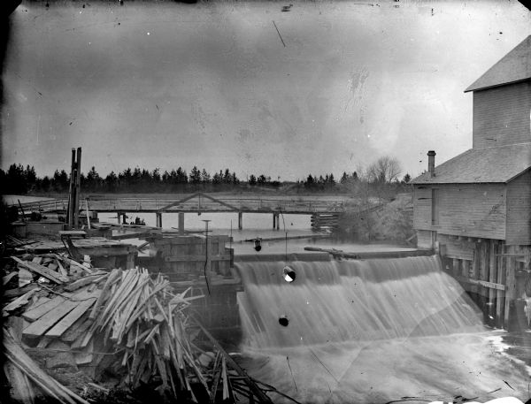 Elevated view of a wooden bridge and dam at Merrilan. Lumber is piled on the left.