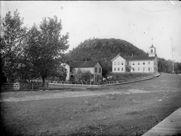 View across field from board sidewalk towards a school near a hill, with an exposed bluff in the background. Identified as the Humbird School in Clark County.