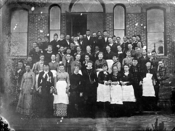 Group portrait in front of the Teachers' Institute. Some of the women in the front are wearing aprons.