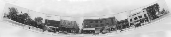 Composite panoramic view of the south side of the 100 block of State Street. Businesses include: Brathaus, The Perfume Shop, Lou's Tobacco Bar, Pattie Wagon, State Barber Shop, Mitchell Official Dispensary, Cardinal Beauty Shop, Redwood and Ross, Rengstorff, The Best Steak House, C.W. Anderes, Barber Shop, and Brown's Book Shop. The Frances Street parking ramp can also be seen down Frances Street. Several pedestrians and parked vehicles can be seen along the street including a U.S. Mail truck and a vehicle marked NCR on the side.
