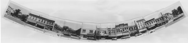 Composite panoramic view of the north side of the 400 block of State Street. Businesses include: Chocolate House, College Boot Shop, Wee-Wash-It, Schwartz Jewelers, Electric Shaver Service and Pen Shop, Tony and Len's Barber Shop, Beecher's Stereo Components and Tape Recorders, Wisconsin Typewriter Co., Army Surplus Store, Harper Method Beauty School, Badger Sporting Goods, Patti Music, Remington-Rand Electric Shavers, Capitol Hearing Aid Center, and Badger Liquor. There is a vacant lot between Wee-Wash-It and Schwartz Jewelers that would become Lisa Link Peace Park. Heavily graffitied barricades surround the lot. Et Cetera Gifts can be seen around the corner on Gilman Street. Pedestrians and automobiles are also visible along the street.