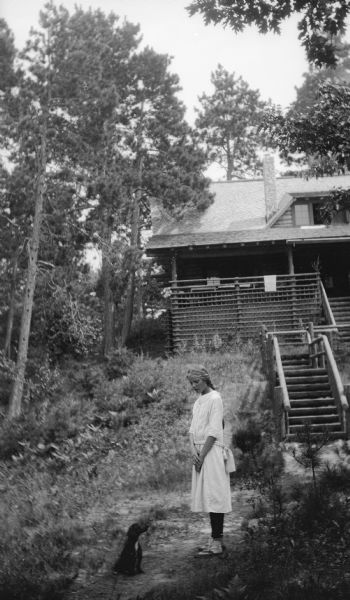 The photographer's daughter Margaret poses with a dachshund on the path in front of the Hotz family cottage on Europe Lake. Two flights of steps on a steep hill lead to the porch with its rustic railing.