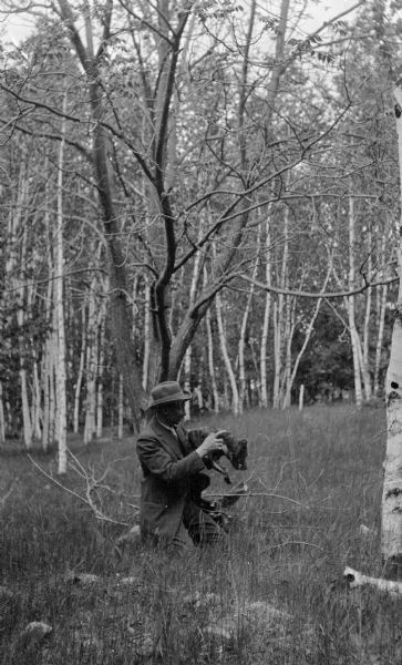 Ferdinand Leonard (Fedy) Hotz poses holding a somewhat uncooperative dog in a stand of birch and other trees.