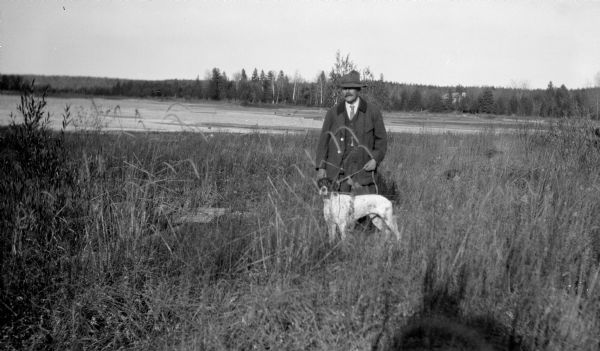 A well-dressed man poses holding a German short-haired pointer on a leash near the outlet of the Fish Creek into the harbor.