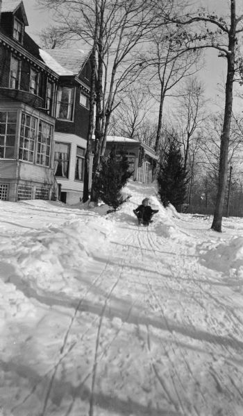 A child in a stocking cap sleds down a course of piled snow at the side of the Hotz family home.