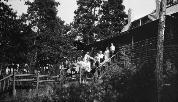 A group poses on the steps leading from the lake path to the porch of the Hotz cottage at Europe Lake. The photographer's daughter, Margaret Hotz, third from right, holds a dachshund.