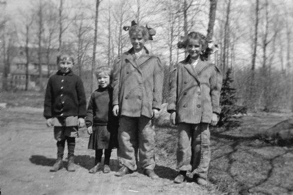 The four children of Ferdinand Hotz, Ferdinand Leonard, Margaret (Sissy), Alice Clothilde, and Helen (Leni), pose for their photograph.  The older two girls wear large bows in their hair, matching suit jackets and pants.
