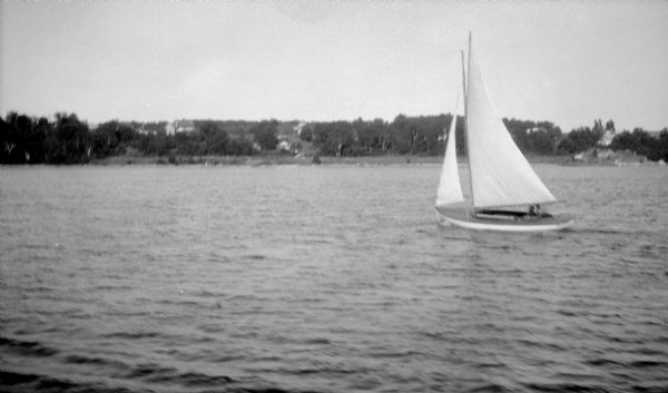 View across water of a small sailboat along the Door County shore.