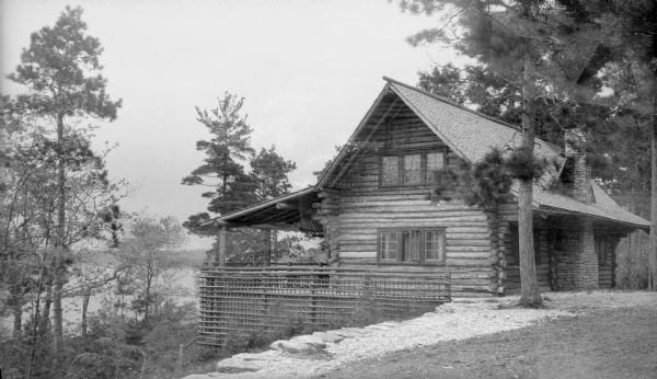 The Hotz family cottage, sited on a hill overlooking Europe Lake, features a large stone chimney, porch, and rustic lattice railing.