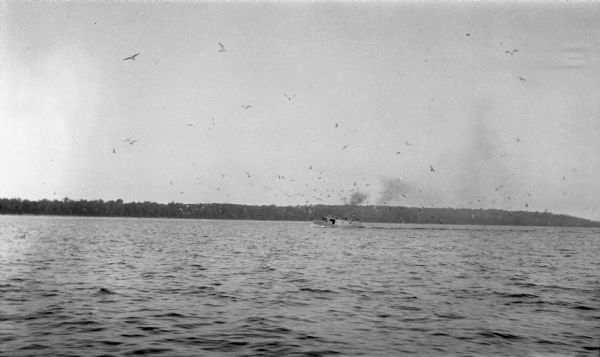 A large flock of seagulls flies over a fishing boat.